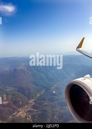 Flugreisekonzept. Wunderschöne Landschaft aus der Luft durch das Flugzeugfenster. Blick aus dem Flugzeug Bullauge. Flugzeugmotor und Blick auf den blauen Himmel. Stockfoto