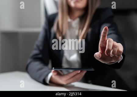 Geschäftsfrau Hält Tablet In Einer Hand Und Zeigt Mit Einem Finger Auf Wichtige Botschaft. Sitzende Frau Im Büro Mit Mobiltelefon In Der Hand Präsentieren Stockfoto