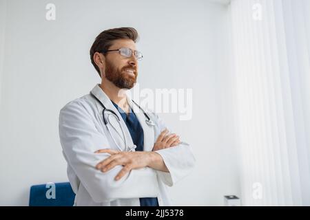 Porträt eines lächelnden Arztes in einer Brille, die in der Medizinklinikhalle steht und wegschaut Stockfoto