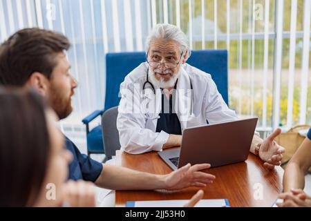 Eine Gruppe von Ärzten, die an einem Tisch im Büro des Krankenhauses sitzen und sich unterhalten Stockfoto