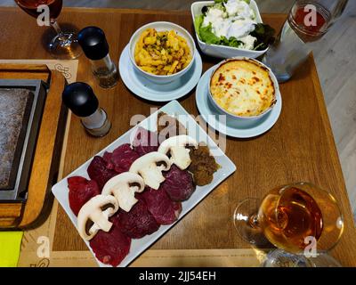 Köstliche verschiedene Arten von Steak mit Pilzen darauf und Kartoffelgratin daneben sind auf einer Platte und bereit, auf einem Steingrill gegrillt werden Stockfoto