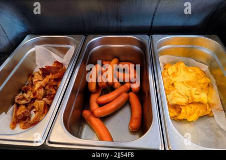 Komplettes englisches Frühstück, bestehend aus Speck, Wurst und Ei in warmen, beheizten Tabletts Stockfoto