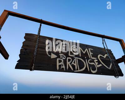 Seitenaufnahme eines hölzernen tropischen Welcome to Paradise Schild mit einem wunderschönen blauen Himmel Hintergrund Stockfoto