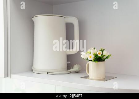 Gemütliche Küche im skandinavischen Stil. Weißer matter elektrischer Wasserkocher und dekorative Blume auf dem Regal. Stockfoto