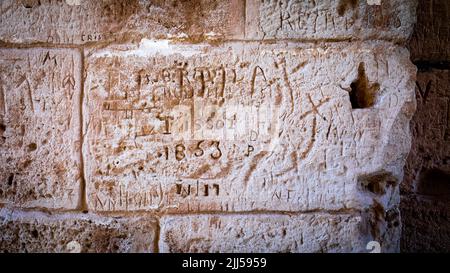 Graiffiti, darunter von einem Mann namens Tissot aus dem Jahr 1853, wurde in eine Wand innerhalb des antiken römischen Amphibitheats in El Jem (Thysdrus) in Tunesien geschnitzt. Stockfoto