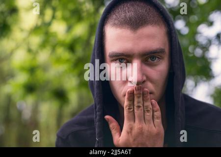 Porträt eines jungen ernsthaften Mannes, der Kapuzenpullover und Hand über Mund trägt Stockfoto