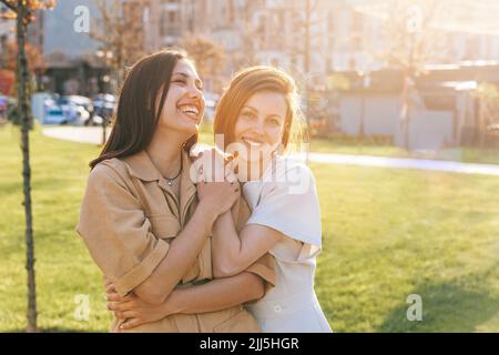 Glückliche Frau umarmt fröhlichen Freund im Park an sonnigen Tag Stockfoto