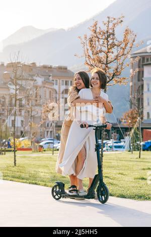 Glückliche Freunde genießen Fahrt auf Push Scooter im Park Stockfoto