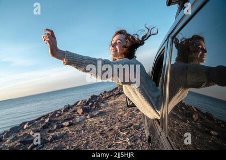 Glückliche junge Frau mit geschlossenen Augen, die sich aus dem Autofenster lehnt Stockfoto