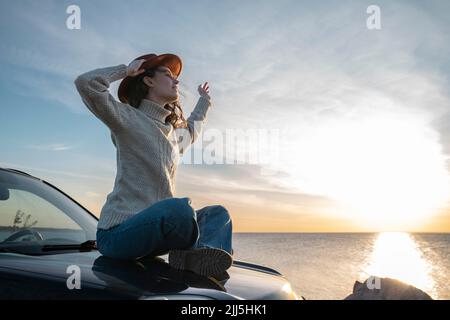 Junge Frau mit Hut auf Autohaube sitzen Stockfoto