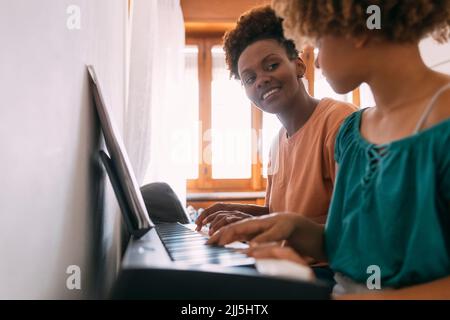 Mutter lehrt Tochter zu Hause Klavier zu spielen Stockfoto