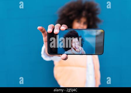 Selfie des Mädchens, das aus der Zunge herausragt, auf dem Bildschirm des Smartphones gesehen Stockfoto