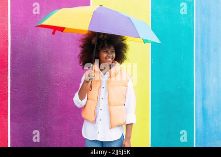 Happy girl steht mit bunten Regenschirm vor der bunten Wand Stockfoto