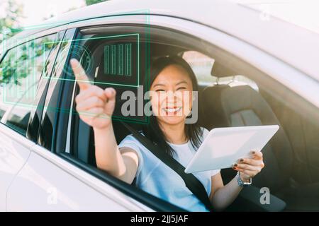 Glückliche reife Frau mit Tablet-PC auf virtuellen Bildschirm sitzen im Auto Stockfoto