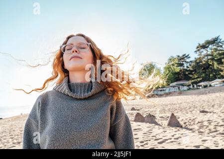 Junge Frau mit geschlossenen Augen genießt frische Luft am Strand Stockfoto