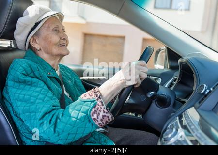 Lächelnde ältere Frau in einem Auto mit Baskenmütze Stockfoto