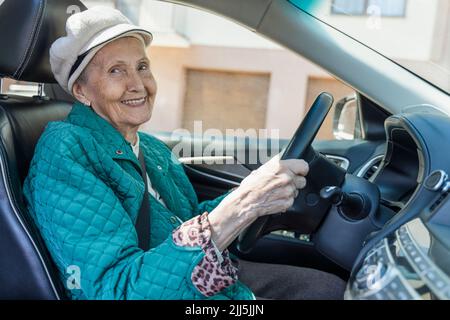 Lächelnde ältere Frau mit Baskenmütze, die im Auto sitzt Stockfoto