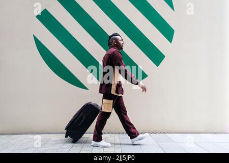 Mann mit Koffer, der an einer Wand auf einem Fußweg läuft Stockfoto