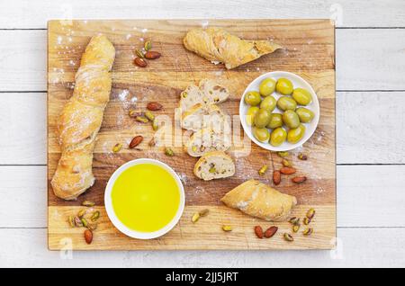 Studio Schuss von Schale mit Olivenöl, grünen Oliven und Laibe von hausgemachtem Pain Paillasse Brot mit Mandeln und Pistazien Stockfoto