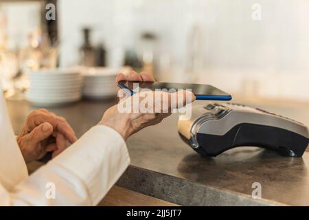 Ältere Frau, die per Mobiltelefon bezahlt Stockfoto