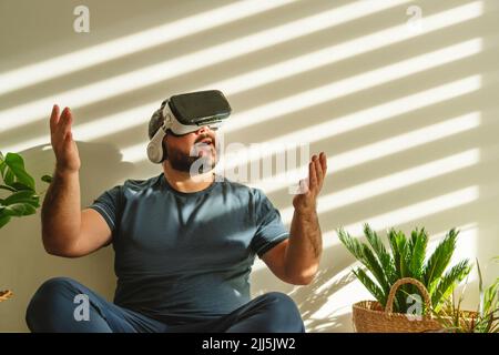 Fröhlicher Mann mit VR-Brille und gestikulierenden Gesten vor der Wand Stockfoto