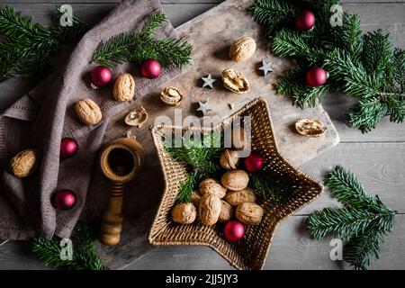 Studioaufnahme von Schneidebrett, sternförmigem Korbkorb, Zweigen, Weihnachtsschmuck, Walnüssen und einfachem Nussknacker Stockfoto