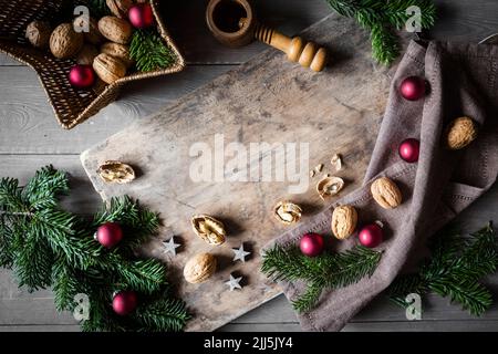 Studioaufnahme von Schneidebrett, sternförmigem Korbkorb, Zweigen, Weihnachtsschmuck, Walnüssen und einfachem Nussknacker Stockfoto