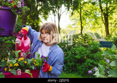 Frau gießt Blumen mit Gießkannen im Garten Stockfoto