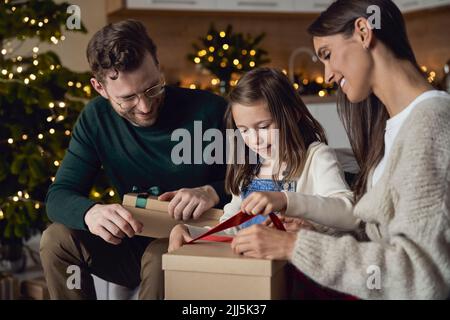 Mädchen Eröffnung Weihnachtsgeschenk sitzen mit Eltern zu Hause Stockfoto