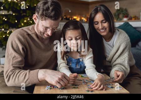 Lächelnde Eltern mit Tochter, die sich zu Hause dem Puzzle anschließt Stockfoto