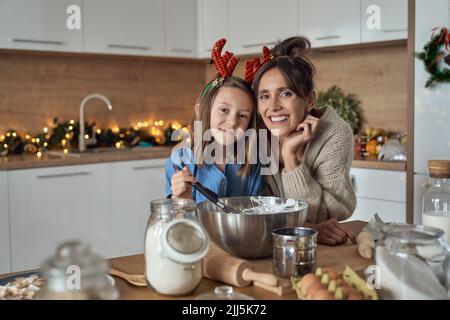 Lächelnde Frau und Tochter mit Rührschüssel in der Küche Stockfoto