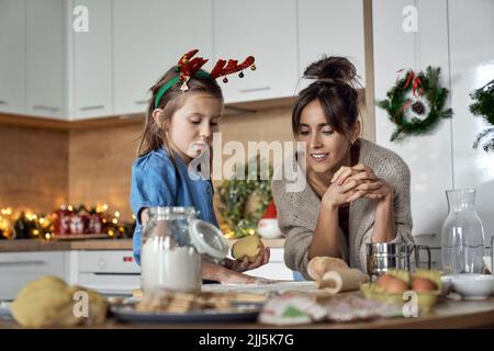 Mädchen, das Keksteig macht, steht von der Mutter in der Küche Stockfoto