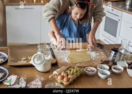 Mutter hilft Tochter im rollenden Plätzchenteig Stockfoto