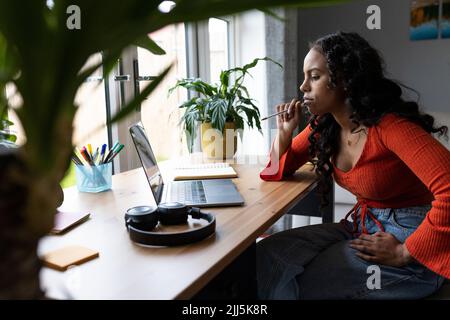 Junge Frau, die am Schreibtisch freiberuflich auf einem Laptop arbeitet Stockfoto