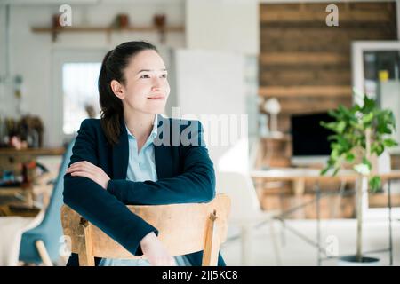 Durchdachte Geschäftsfrau, die im Büro auf einem Stuhl sitzt Stockfoto