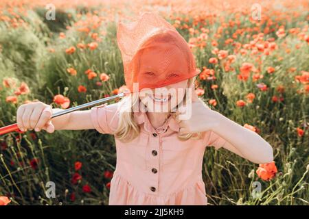 Spielerisches Mädchen spielt mit roten Schmetterlingsnetz in Mohn Feld Stockfoto