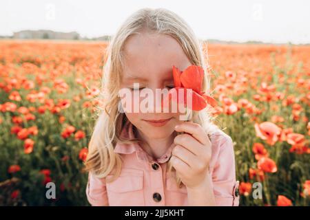 Mädchen, das Auge mit roter Blume im Feld bedeckt Stockfoto