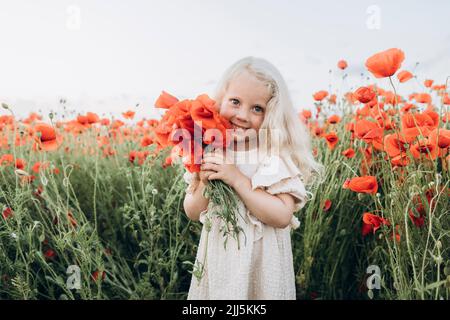 Lächelndes Mädchen hält rote Blume in Mohnfeld Stockfoto