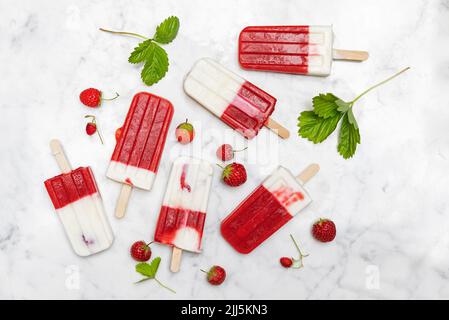 Hausgemachte Erdbeer-Joghurt-Popsicles, flach auf weißem Marmor ausgelegt Stockfoto