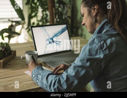 Freiberuflicher Mitarbeiter, der im Heimbüro mit einer Skizze für die Windenergieanlage auf dem Laptop-Bildschirm Notizen macht Stockfoto