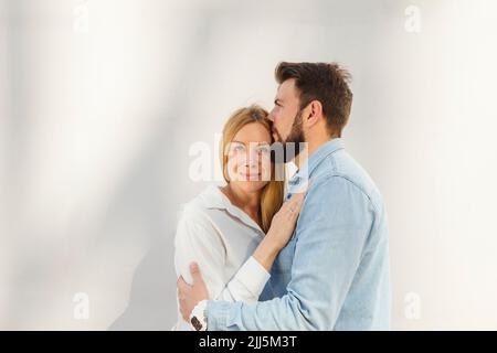 Mann umarmt blonde Frau, die vor der Wand steht Stockfoto