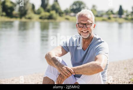Lächelnder älterer Mann mit Brille am Flussufer Stockfoto
