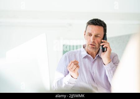 Besorgter Geschäftsmann, der im Büro auf dem Smartphone spricht Stockfoto