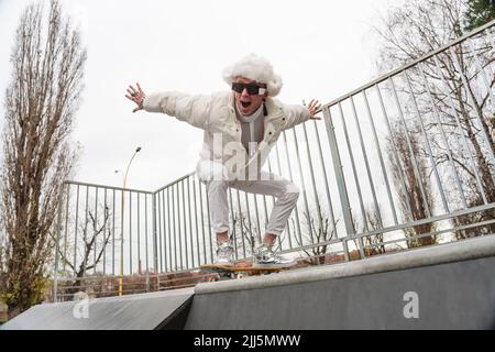 Glücklicher Mann mit offenem Mund balanciert auf Skateboard durch Geländer Stockfoto