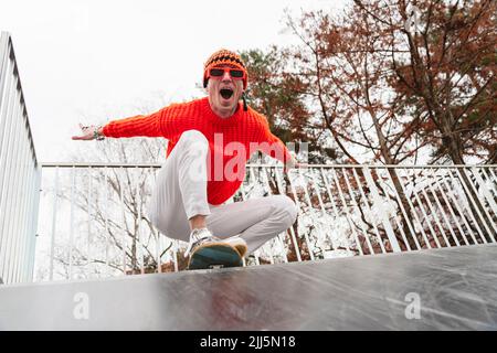 Glücklicher Mann mit ausgestreckten Armen, der vor dem Geländer auf dem Skateboard hockt Stockfoto