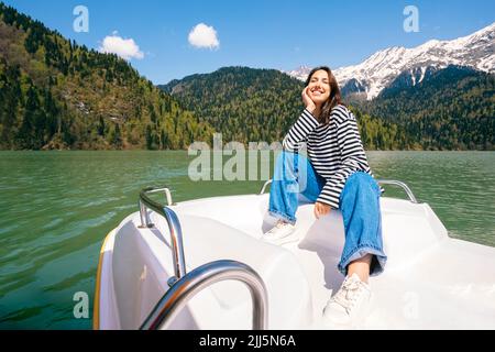 Glückliche junge Frau genießt es, auf dem Boot am See Ritsa zu sitzen Stockfoto
