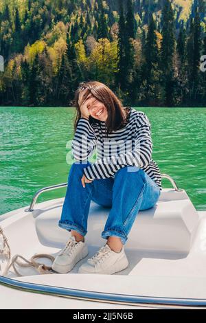 Glückliche junge Frau, die mit dem Kopf in den Händen auf dem Boot am See Ritsa sitzt Stockfoto