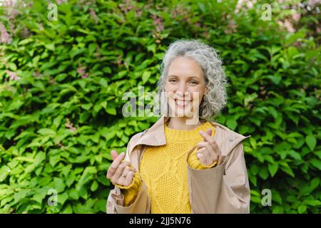 Glückliche Frau, die im Park mit den Fingern Herz formt Stockfoto