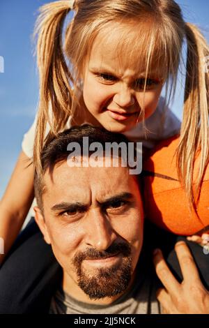 Mann macht Gesicht mit Tochter auf den Schultern sitzen Stockfoto