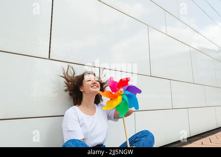 Happy Teenager-Mädchen mit bunten Windrad Spielzeug sitzt vor der Wand Stockfoto